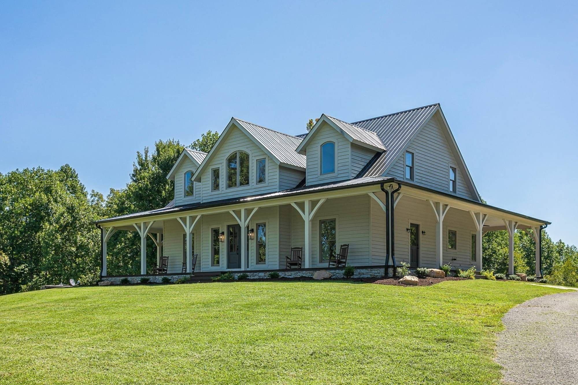 White farmhouse with wraparound porch and metal roof on a hilltop lawn in Williamson County