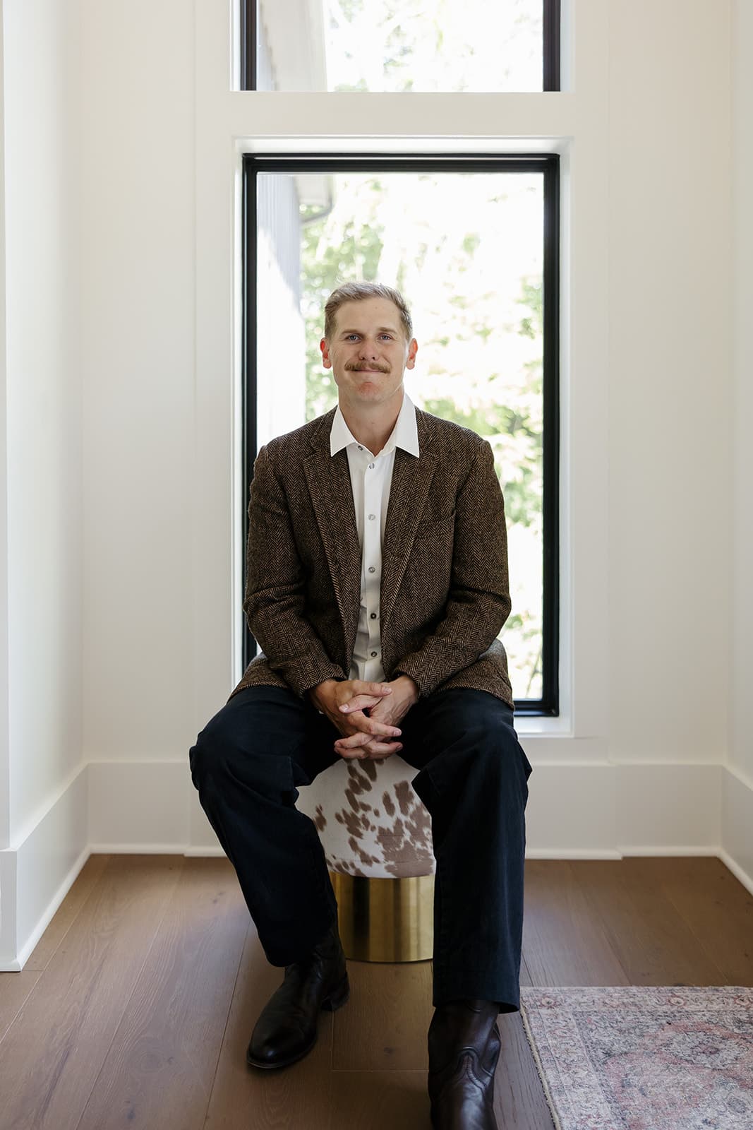 Ryan Boggs seated in a sunlit window nook wearing a tweed blazer