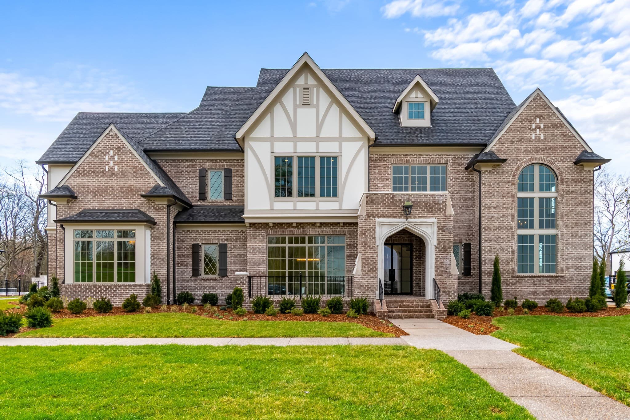 Brick and stucco Tudor-style estate with a steep slate-gray roof and arched stone entry in Franklin, Tennessee